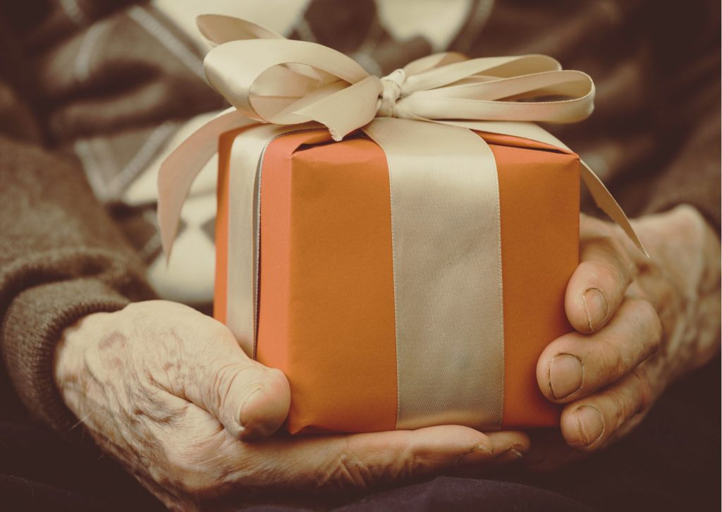 older man's hands holding a gift wrapped with orange paper and a gold coloured ribbon