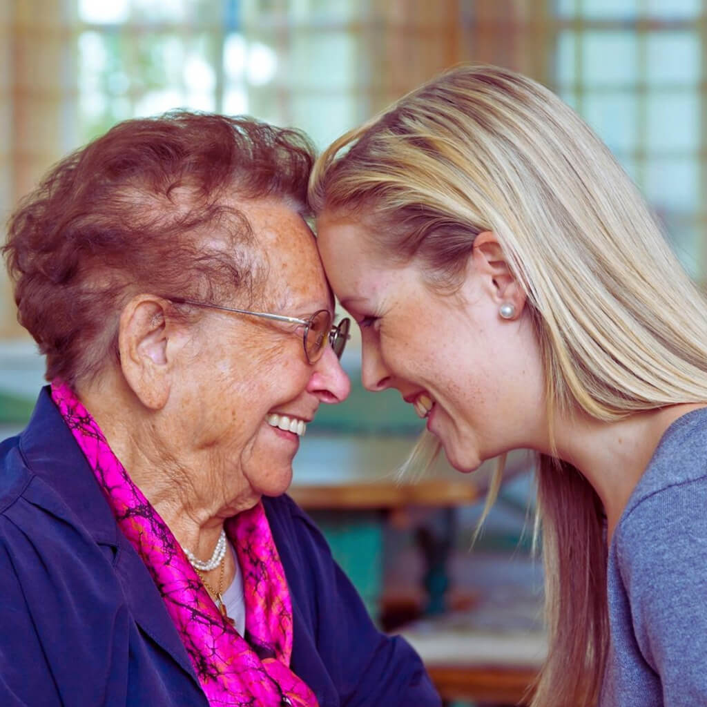 younger woman and older woman smiling while pressing their foreheads together.